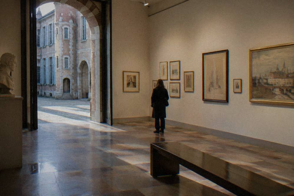 A gallery interior with framed artworks and drawings hung on a pale wall under soft lighting