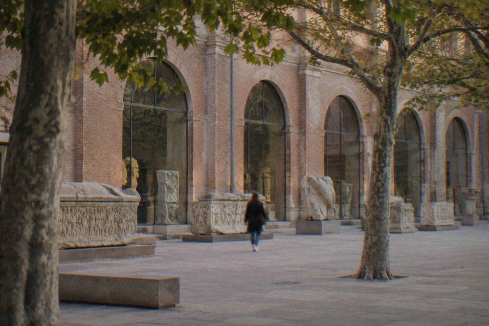 Stone sarcophagi and carved Roman fragments displayed in a gallery with arched windows