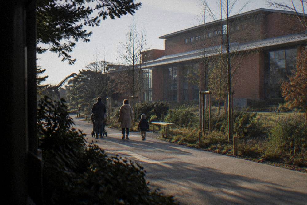 A family walking along a garden path with a large brick museum building in the background