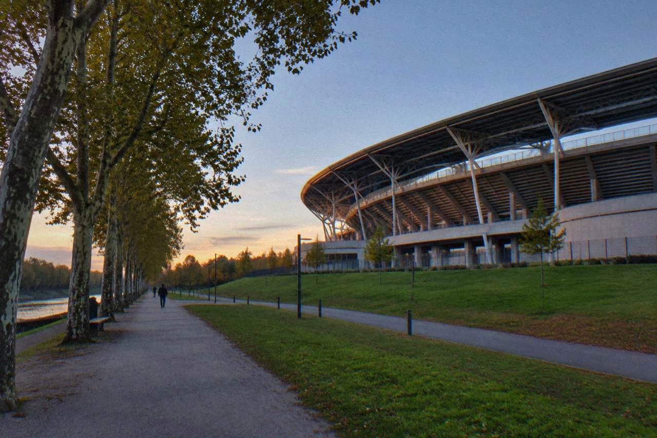 A large modern stadium seen from outside, with its curved stands rising above surrounding lawns and walkways
