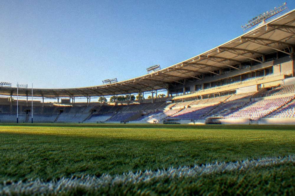 A stadium pitch under a clear blue sky with sunlight on the seats