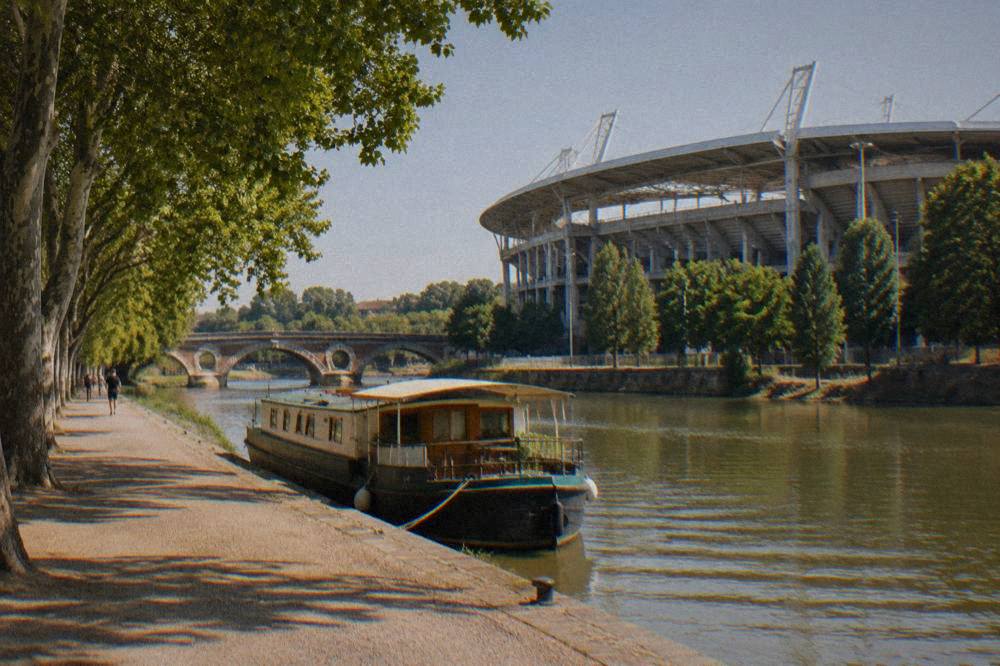 A canal boat moored beside a stone-edged waterway with an old bridge in the background