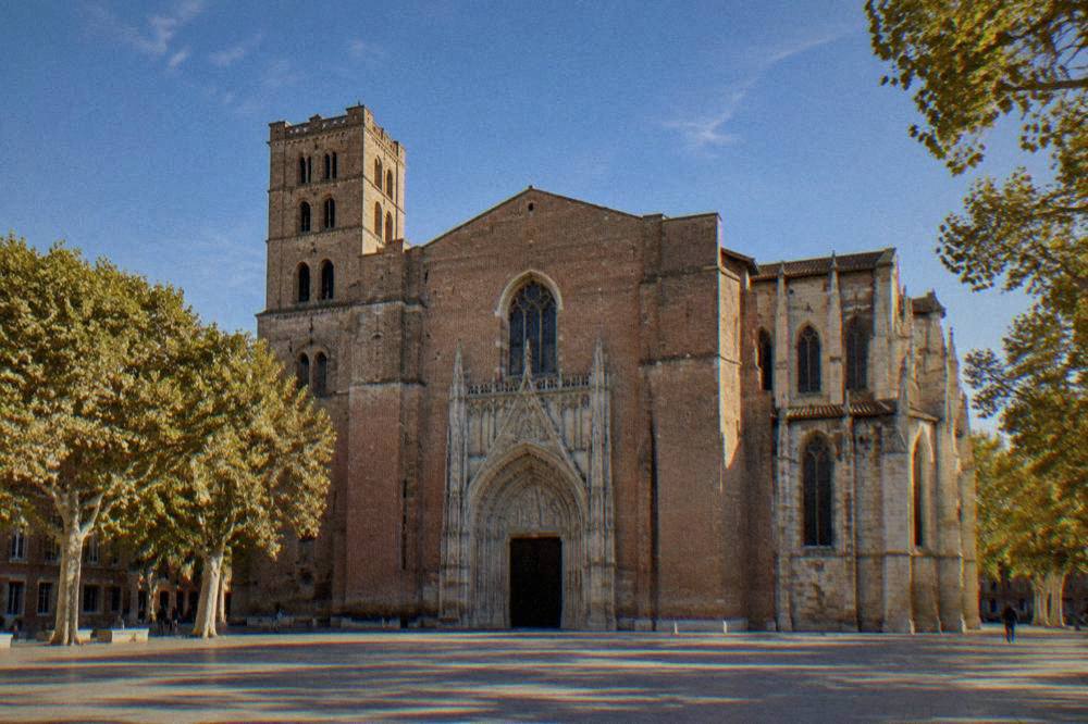 The single doorway of Toulouse Cathedral's wide brick facade with the rose window above