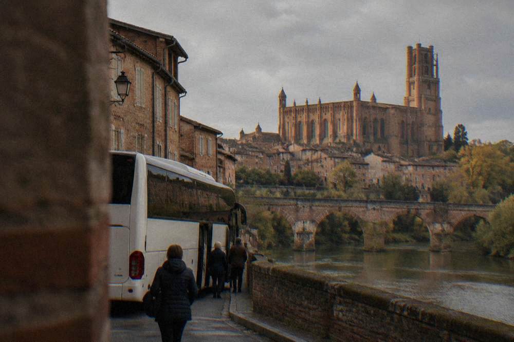 A tour coach parked on a street with medieval brick buildings in the morning light