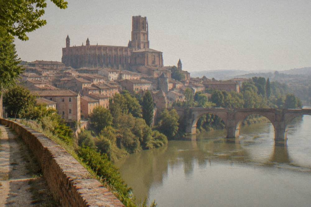 The brick cathedral of Albi rising above rooftops seen from a riverside path