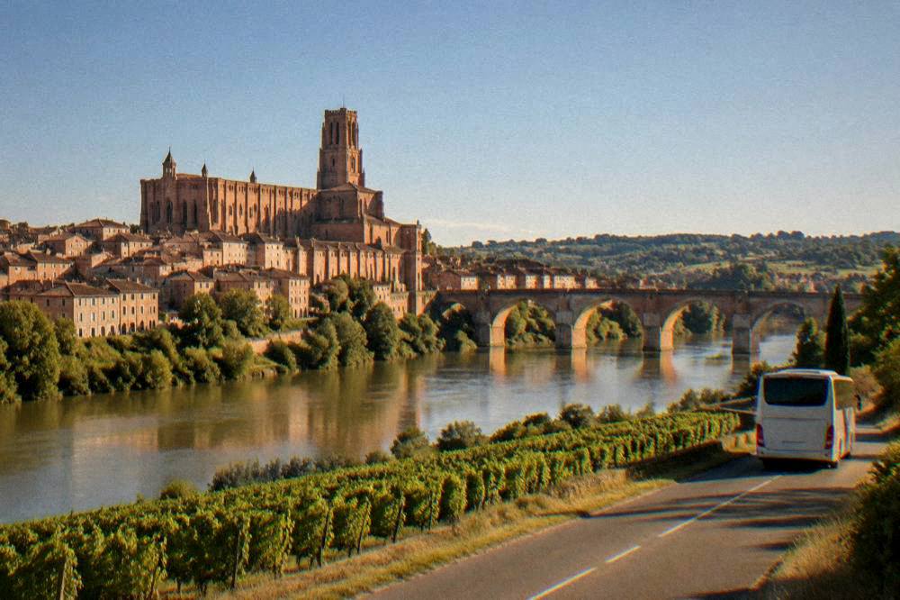 A coach driving on a country road between vineyards and rolling hills in southern France