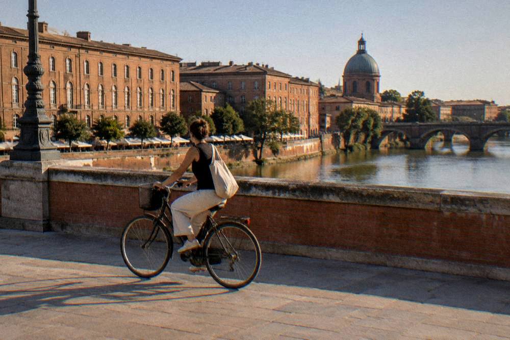A cyclist crossing a Toulouse bridge with pink brick buildings behind