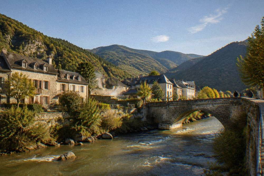 A stone bridge over a fast mountain river with forested slopes behind
