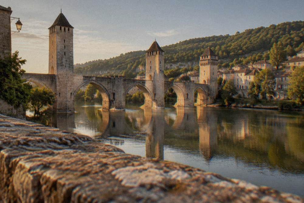 A stone bridge with pointed arches reflected in a slow river at golden hour