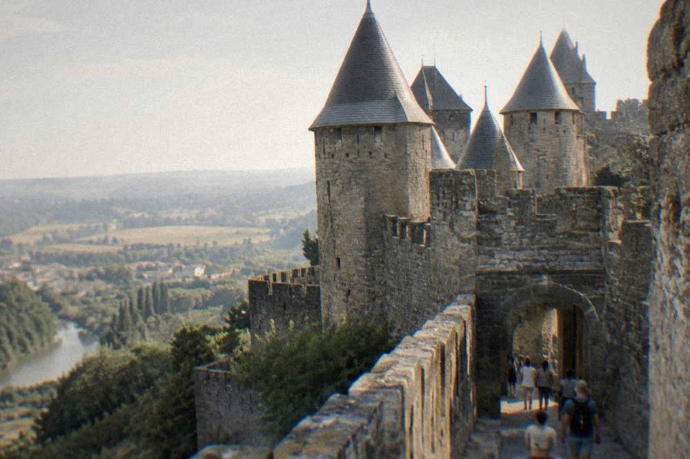 Stone gateway and towers of a medieval fortress entrance with visitors walking through