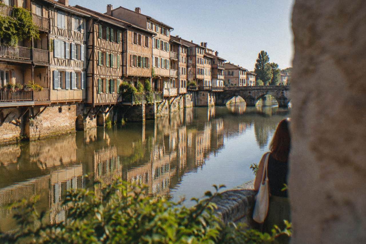 Half-timbered houses with painted shutters reflected in a calm river running through a southern French town
