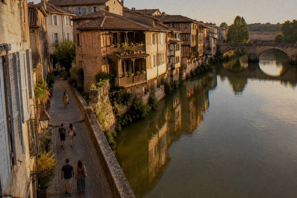 Travelers strolling a narrow old street with shuttered stone facades in a French town
