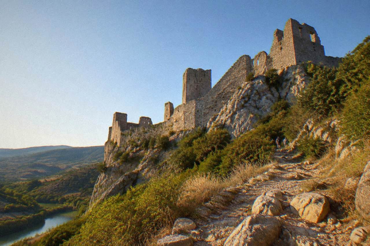 A stone fortress wall rising above a green valley in southern France under a clear sky