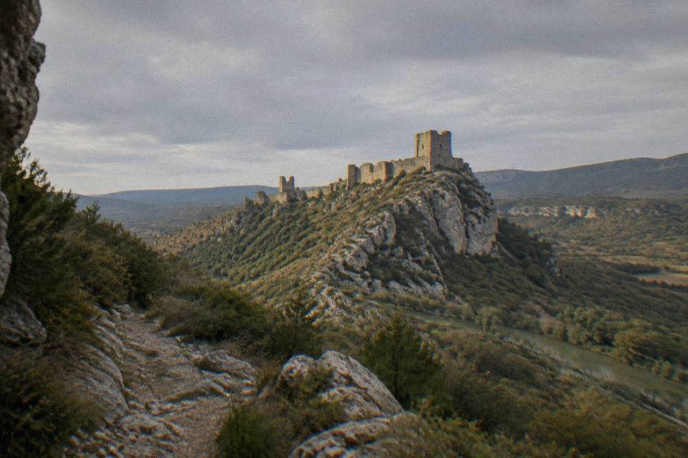 A medieval stone keep on a rocky hilltop seen from a distance across wooded countryside