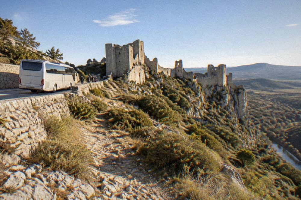 A tour coach parked on a road beside old stone ramparts in the morning light