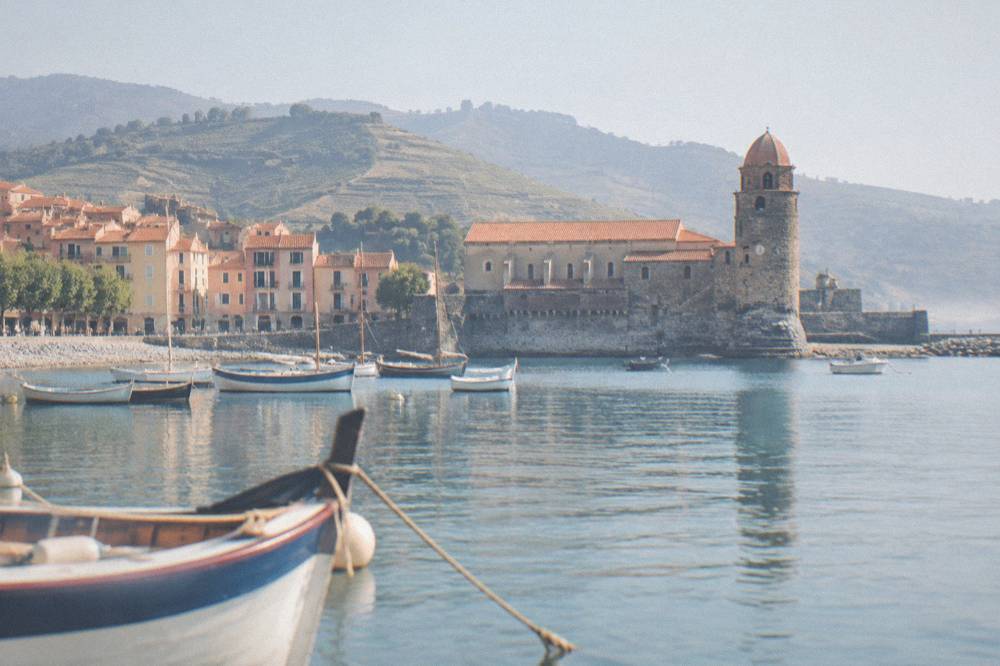 A red and gold church bell tower beside a calm sea with small boats moored nearby