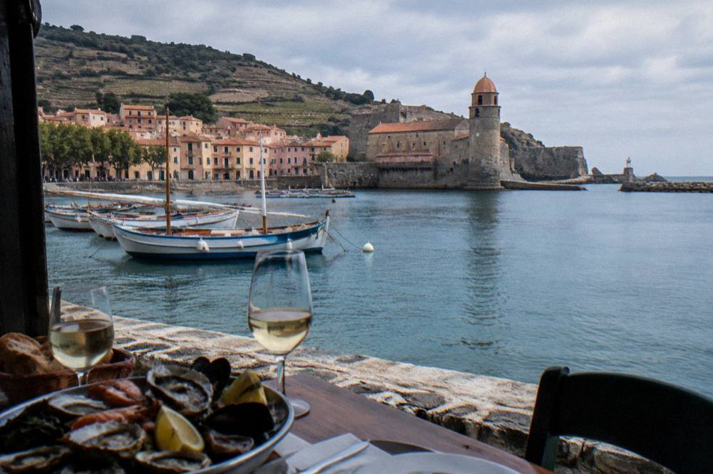A table with wine glasses and a seafood platter beside a harbor view