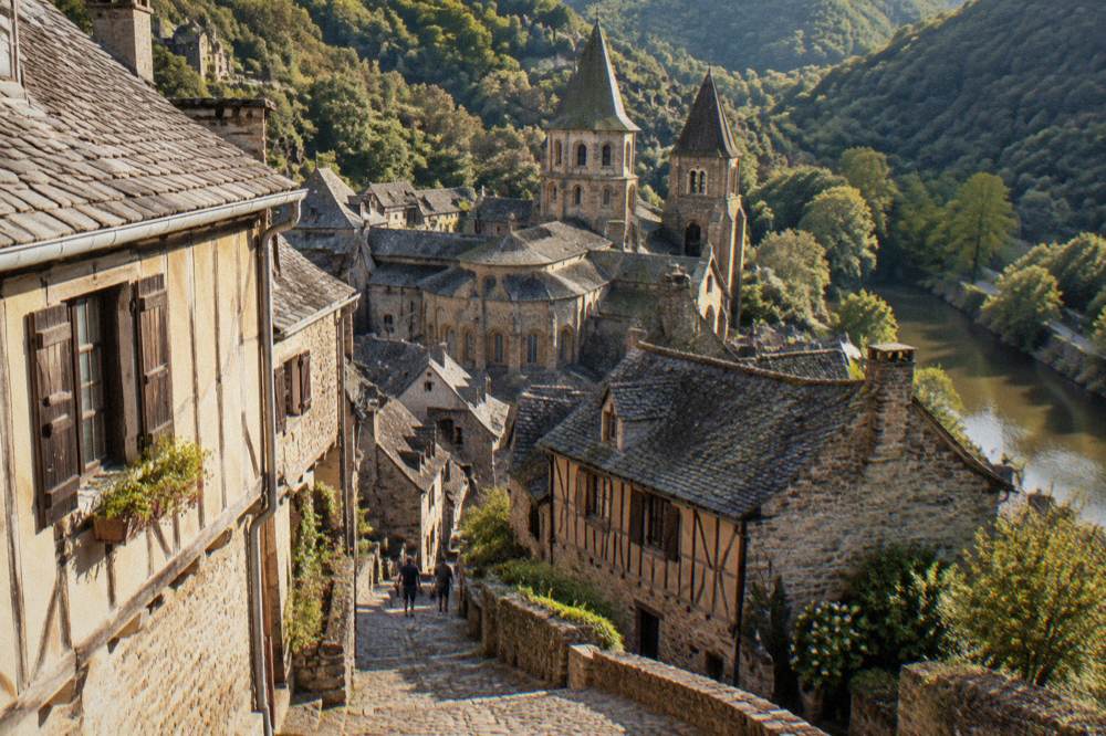 Half-timbered houses on a sloping street in Conques with the abbey towers behind