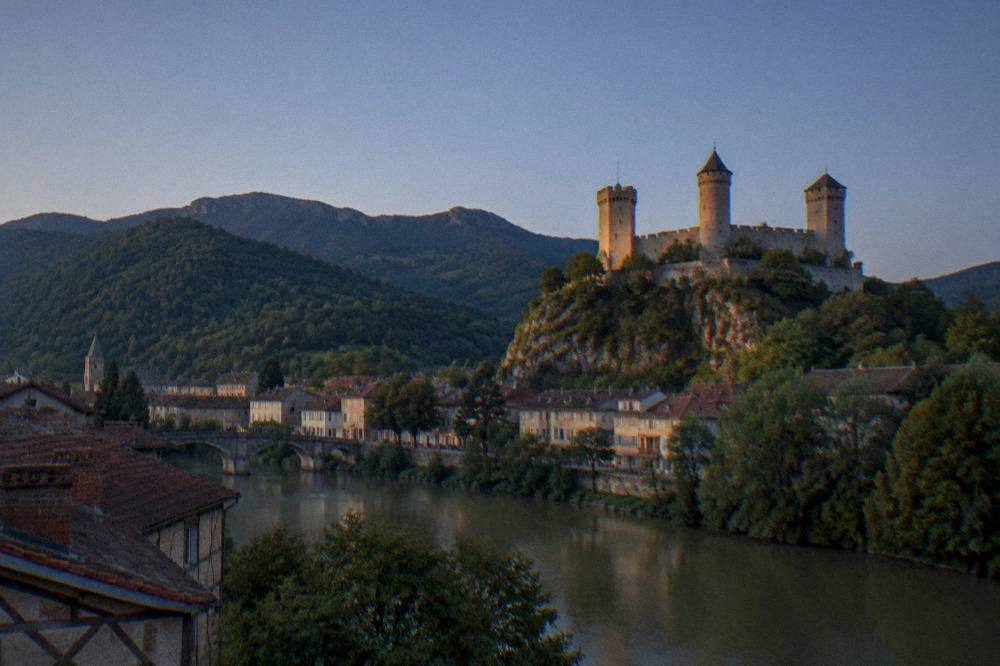 A castle tower seen across a valley with green forested hills under a clear sky