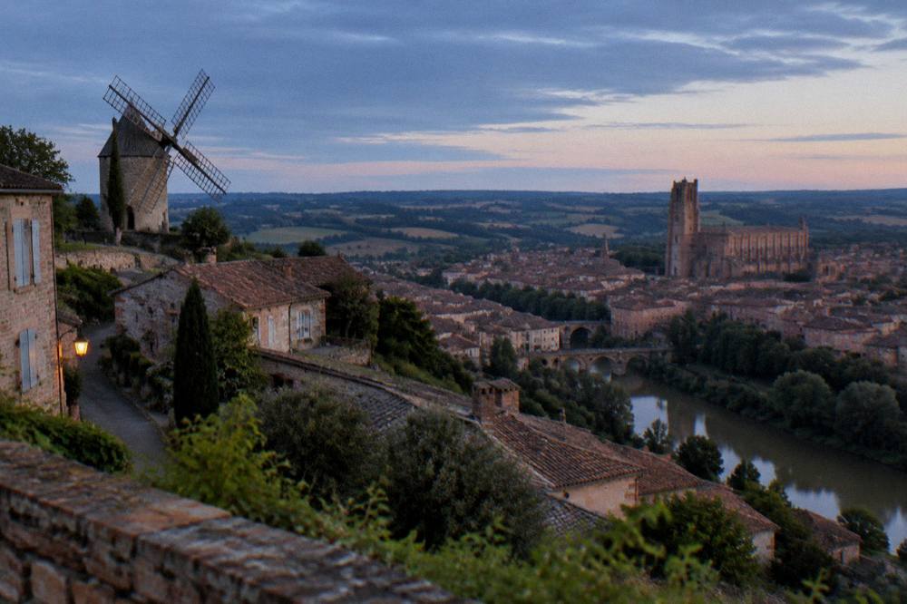 A brick cathedral towering over a red-roofed city beside a river in the Tarn