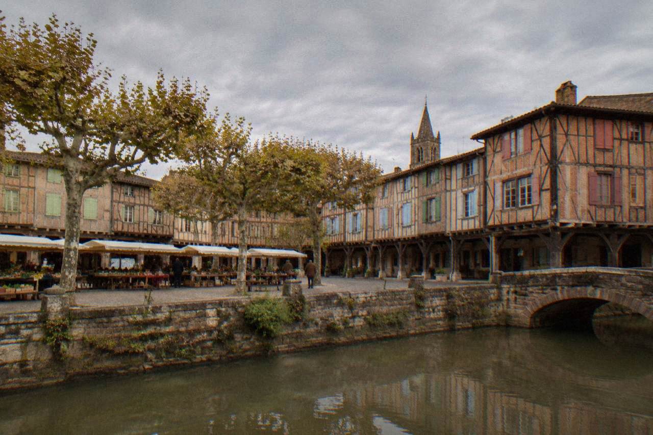 Timber-framed houses with painted shutters rising above the arcades of a medieval market square