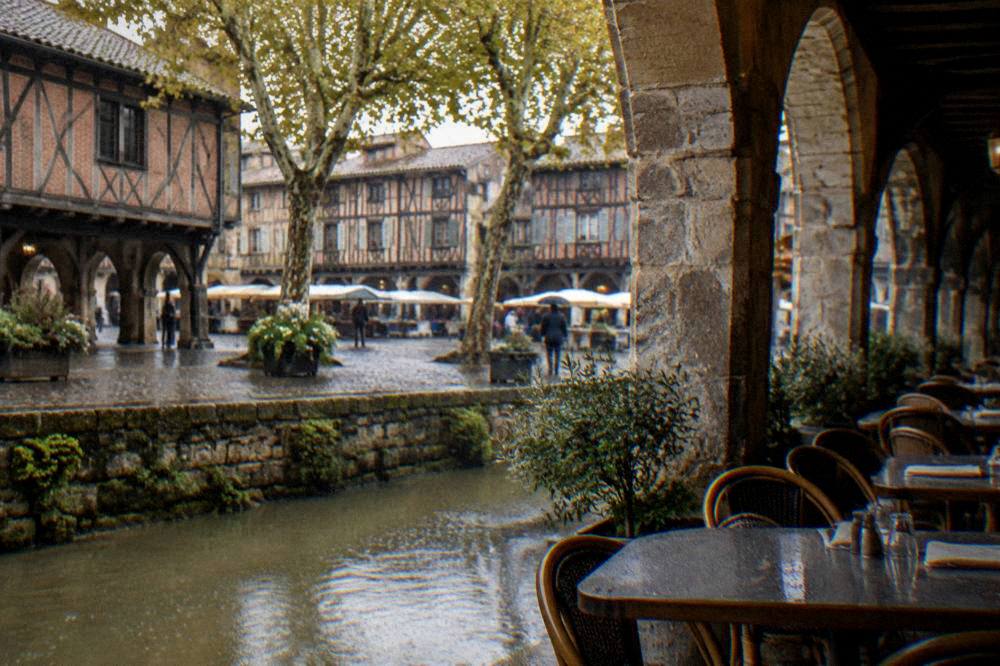 A restaurant terrace with tables set under stone arcades beside a medieval square