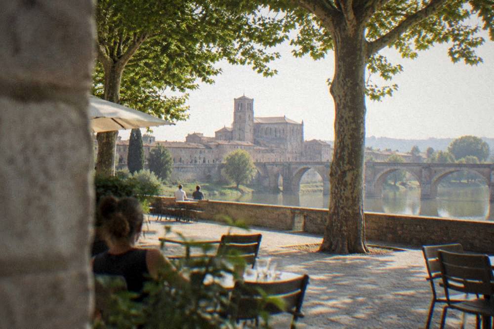 A quiet stone square in Moissac with cafe tables under plane trees in afternoon light