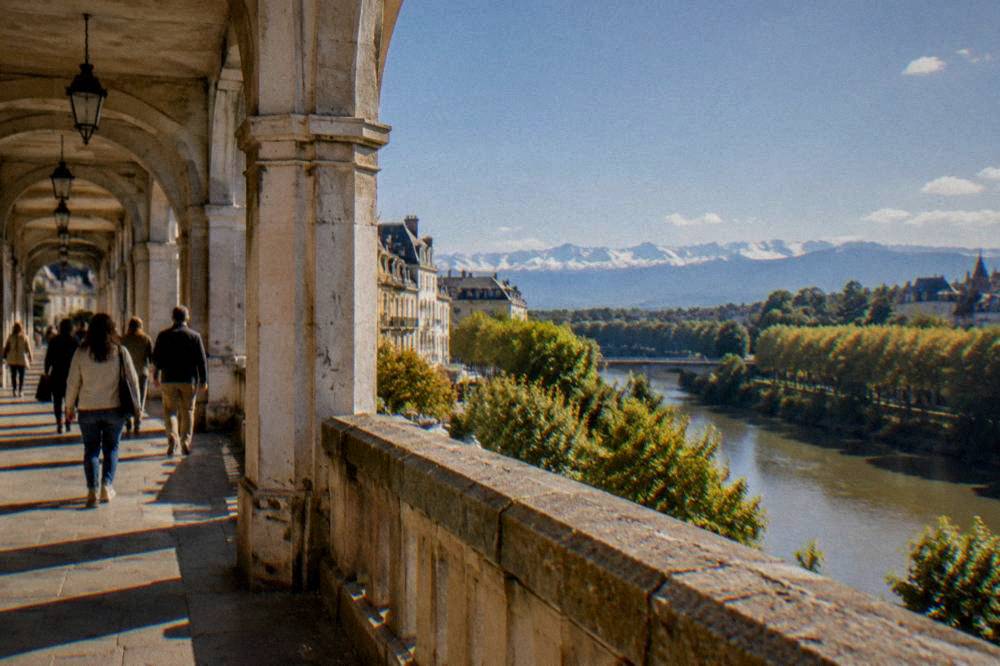 People strolling under the stone arcades of a street in Pau's historic center