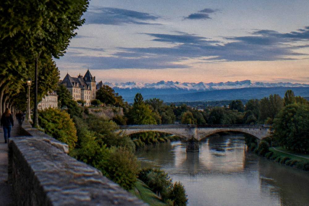 A stone bridge crossing the Gave de Pau river with green banks on both sides