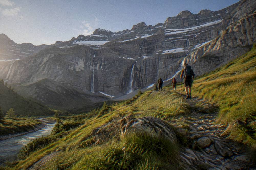 Hikers with backpacks walking a high grassy ridge with mountain peaks behind them