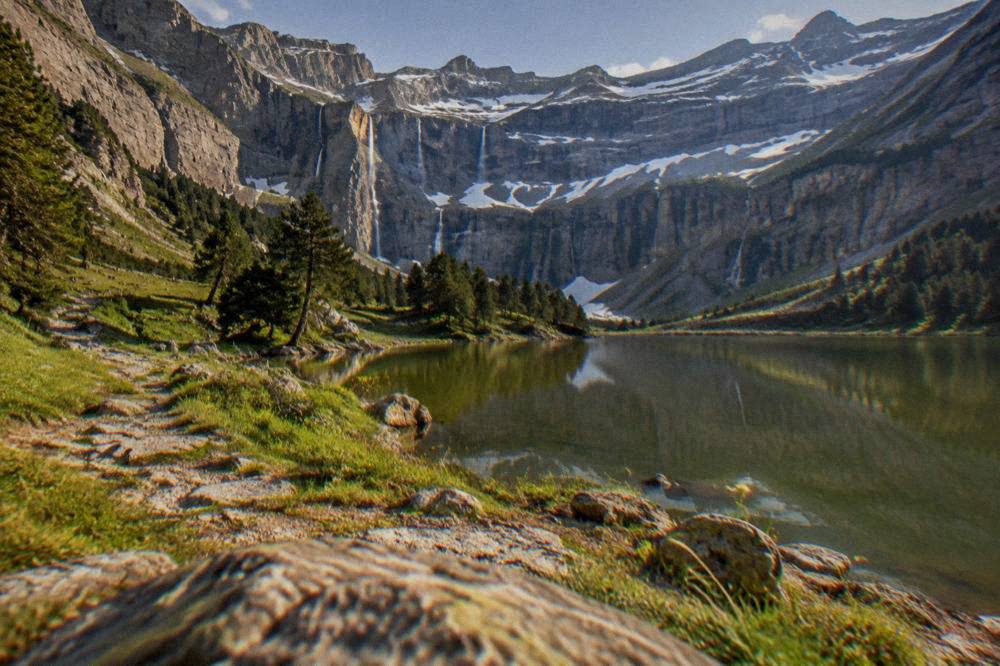 A mountain lake reflecting jagged peaks, with pine trees along the shoreline