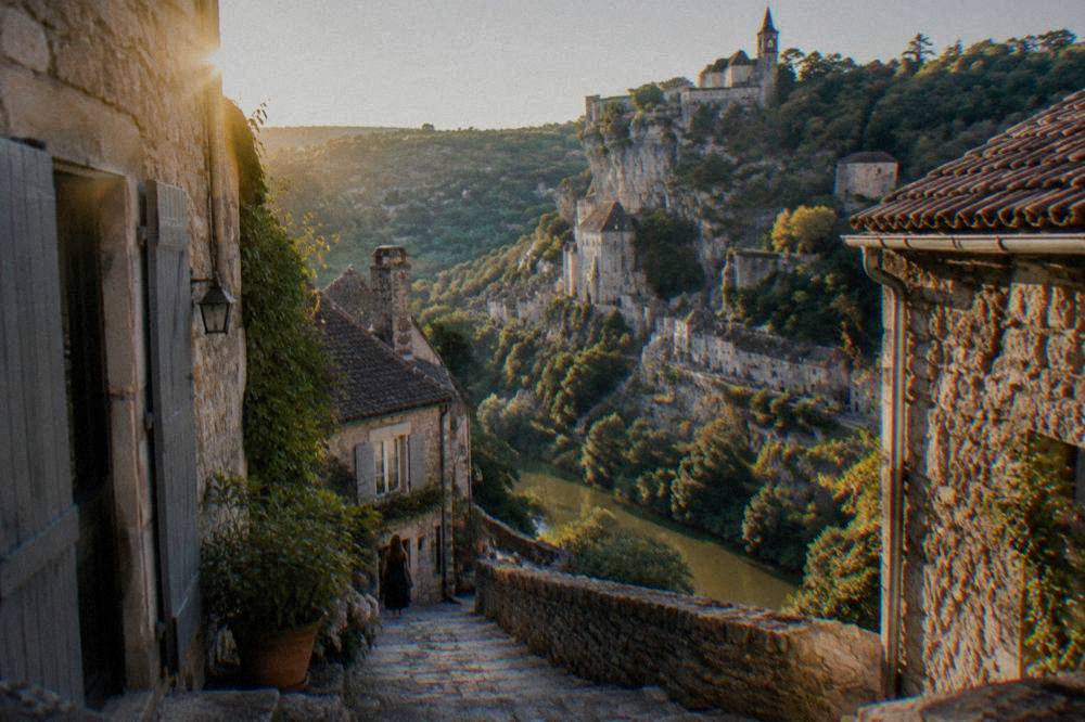 A narrow stone lane in a cliff village with old houses on both sides and a view of the gorge beyond.