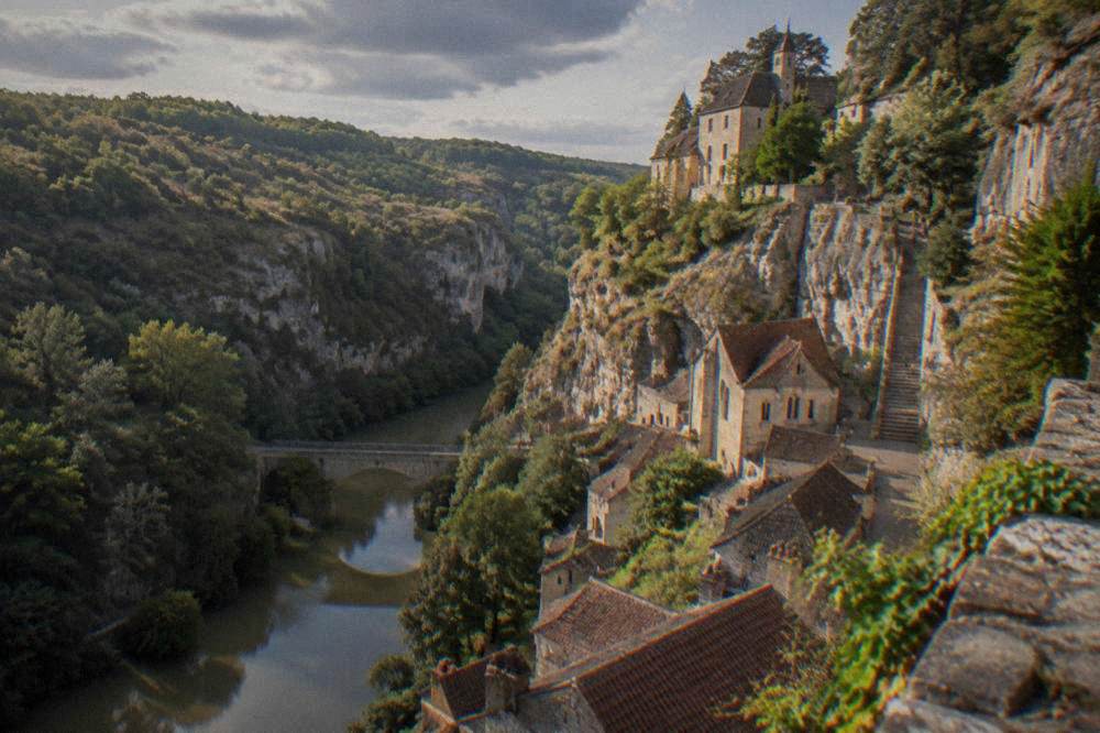 A small stone bridge over a river gorge with wooded cliffs rising behind it.