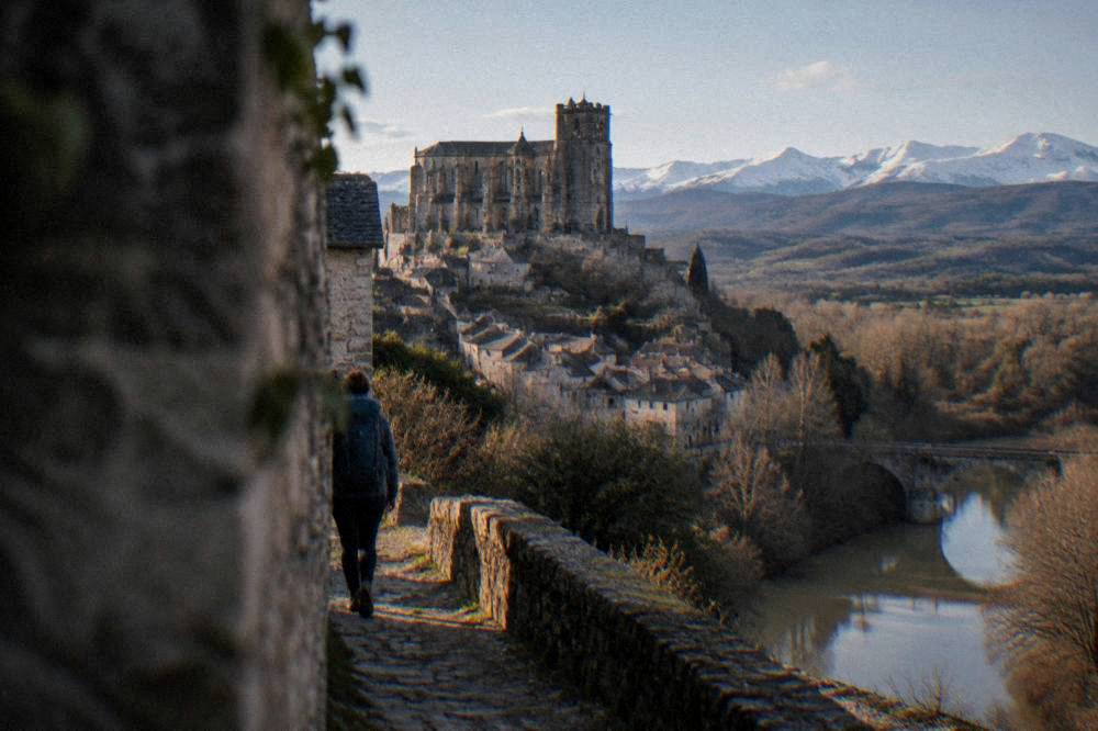 A hiker with a backpack walking a stone path toward a village on a ridge