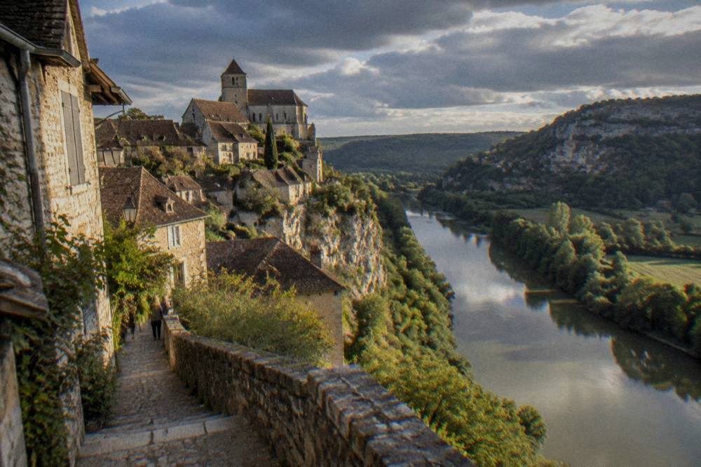 A river flowing between wooded hills with a village visible on a distant cliff