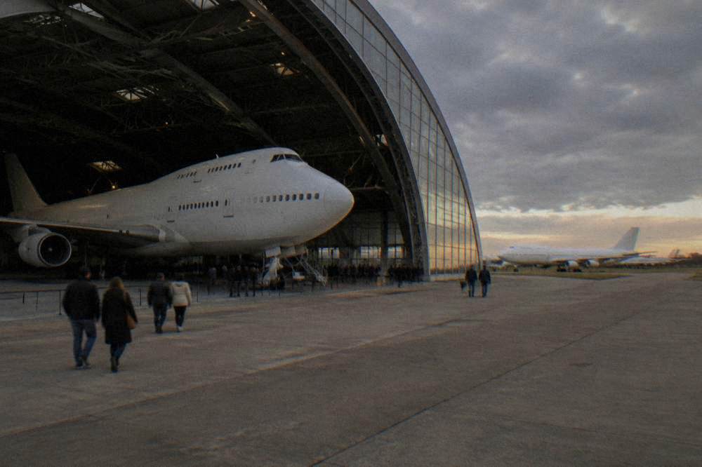 Visitors walking beneath a full-size retired airliner inside a museum hangar