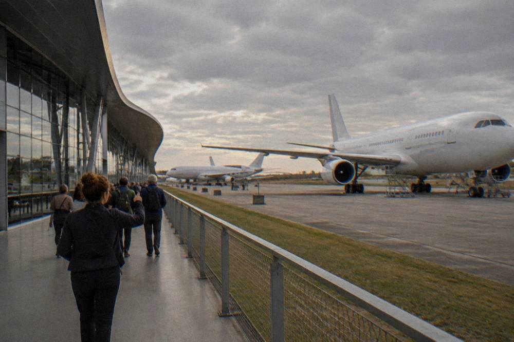 Guide leading a small group of visitors along a walkway beside an aircraft assembly line