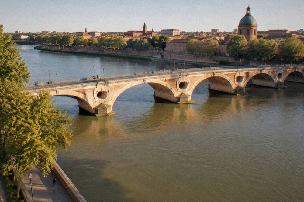 The Garonne river and Pont Neuf bridge in Toulouse under a clear sky