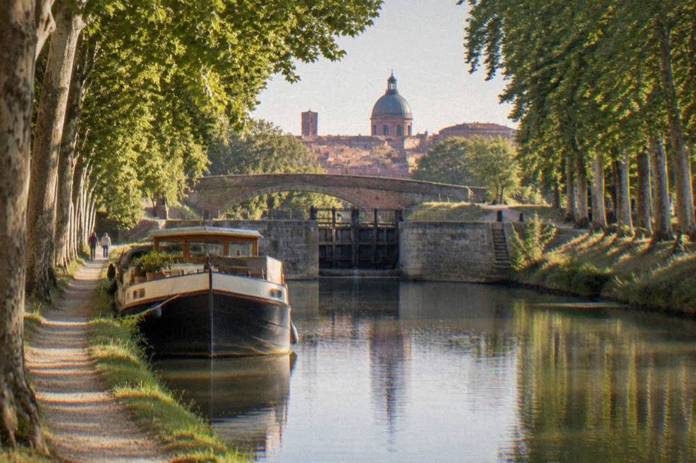 A moored canal boat at a Toulouse canal basin with the city behind