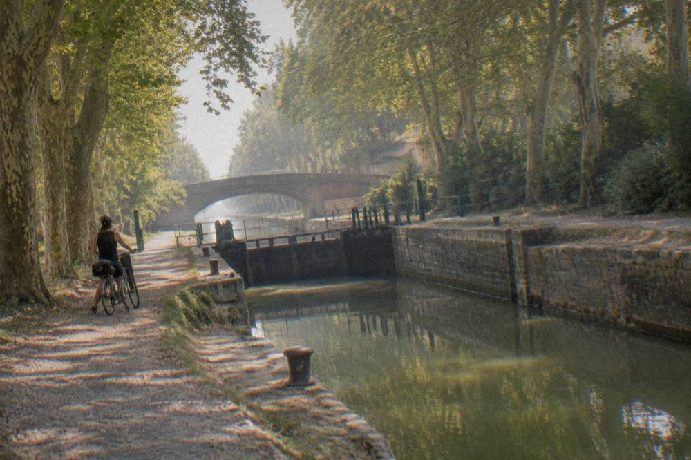A canal lock with stone walls and calm green water, with a cyclist waiting at the towpath edge