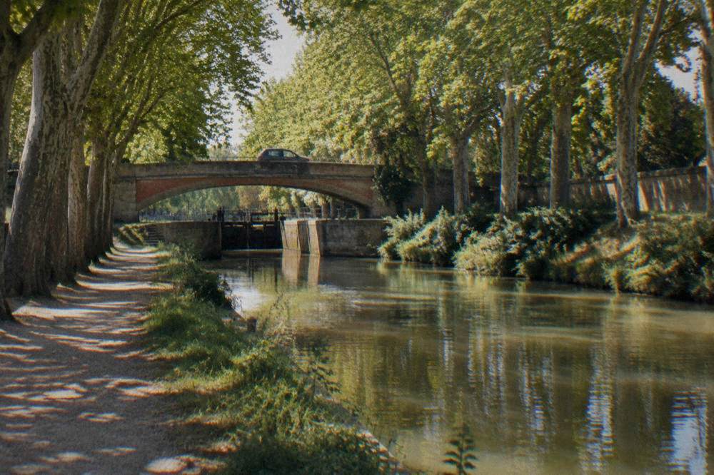 A car parked on a stone bridge over the Canal du Midi with plane trees along the banks