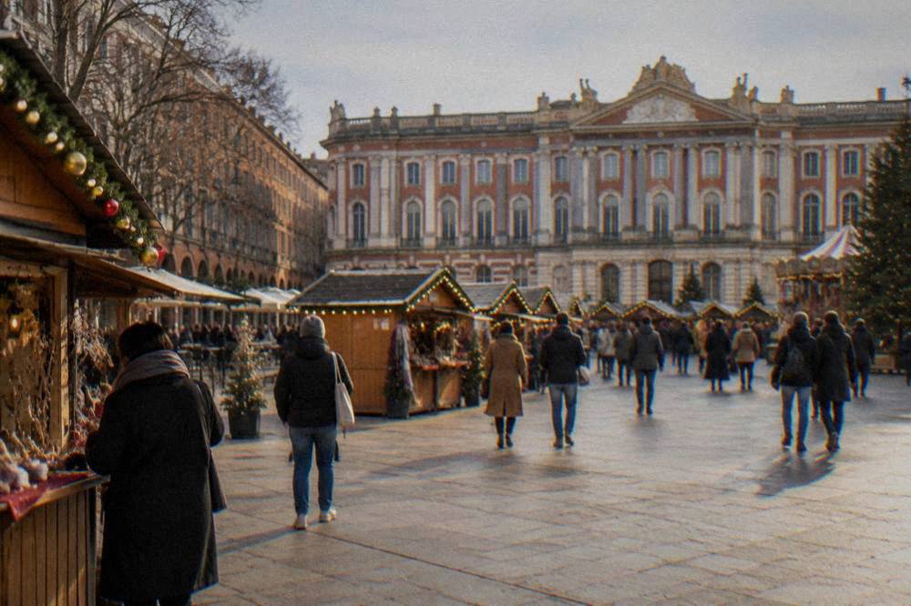 A Christmas market with wooden chalets and lights in front of the Capitole building in Toulouse