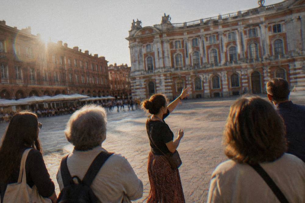 A guided walking group standing in a Toulouse square with a guide gesturing toward a historic building