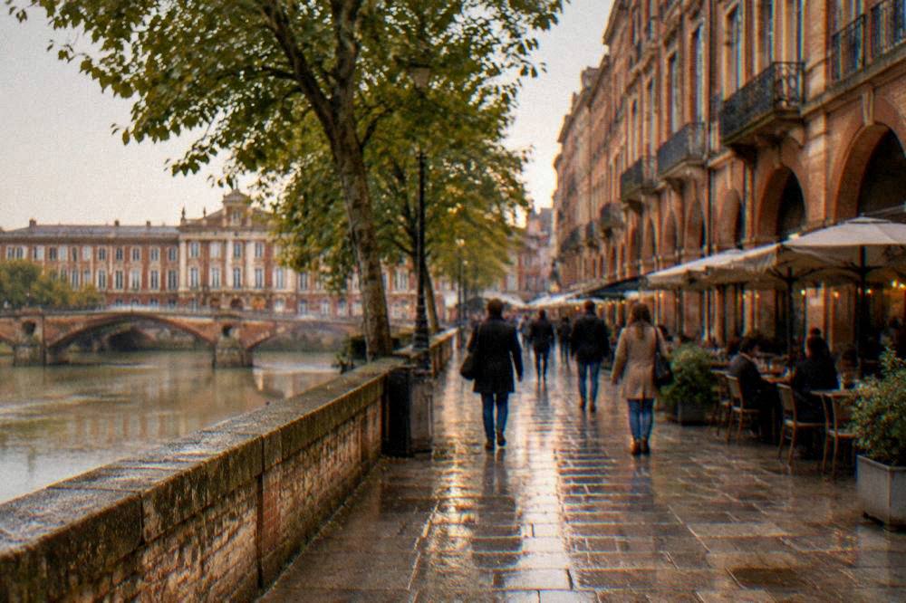 A pedestrian street in central Toulouse with pink-brick facades and people strolling past cafe tables