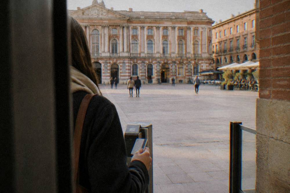 A visitor holding a transport pass at the entrance of a Toulouse museum with a pink-brick courtyard beyond