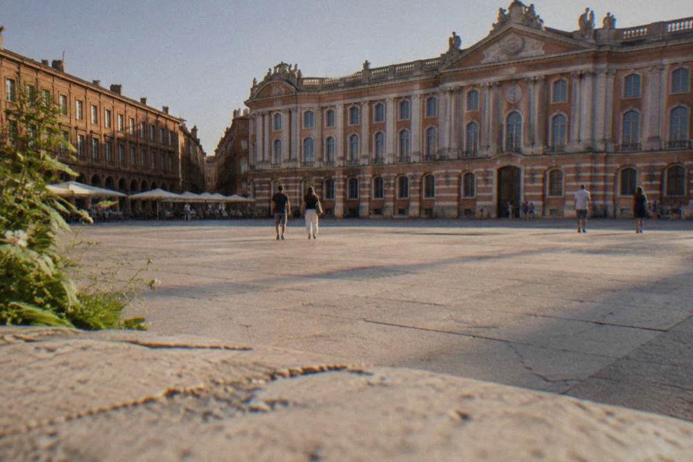 A wide plaza in front of a grand brick palace building in Toulouse