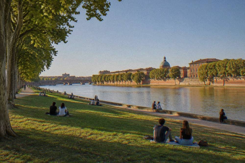People relaxing on the grass of the Prairie des Filtres park beside the Garonne river in the evening