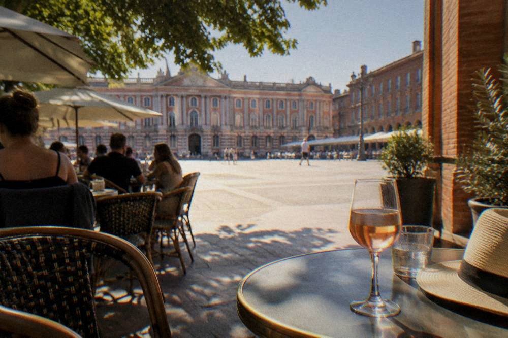 A sunny summer evening on a Toulouse terrace with cafe tables and pink brick walls