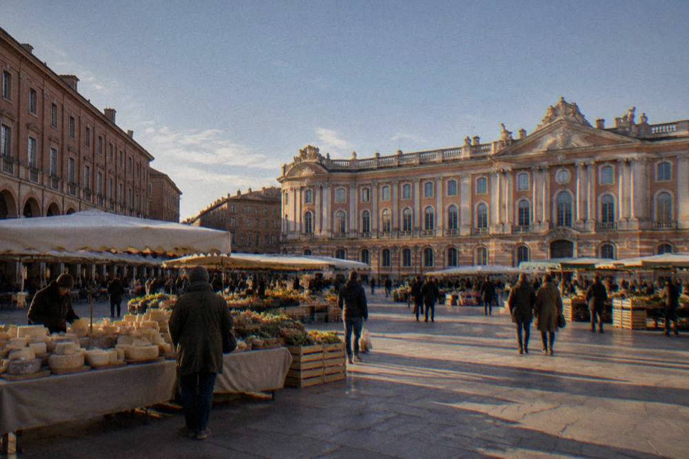 Stall holders and shoppers at an outdoor food market in Toulouse with cheese and produce on display