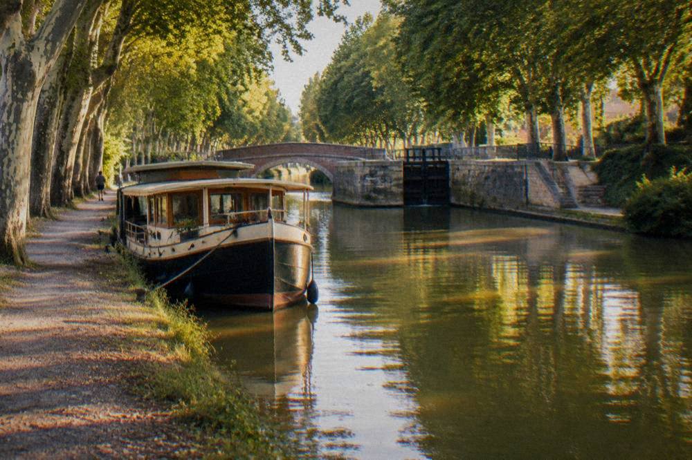 A canal boat moored on the Canal du Midi with plane trees along the bank